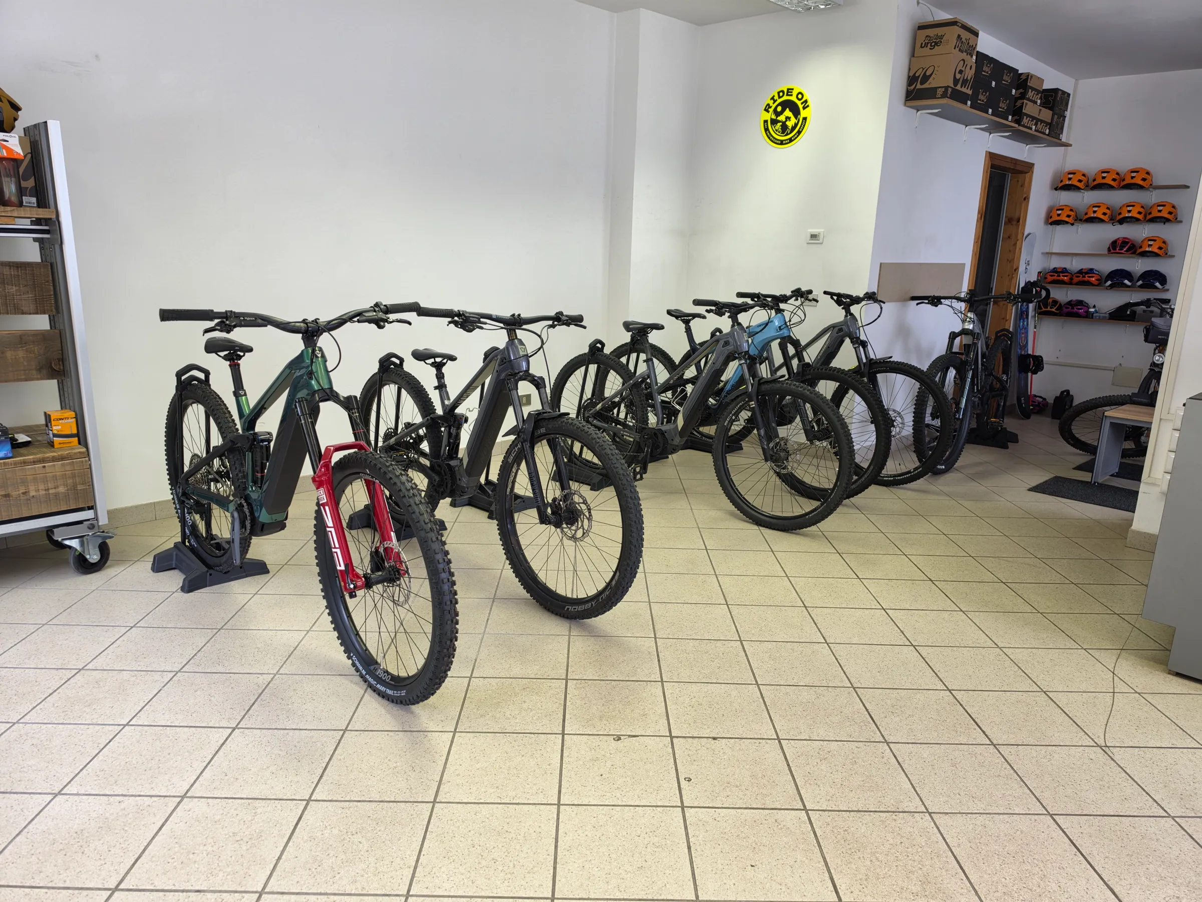 Interno del negozio RIDE ON: e-MTB in fila, caschi arancioni a muro e insegna gialla